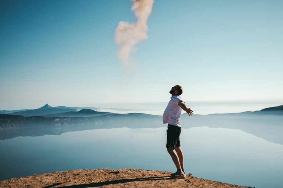 Un homme écartant les bras devant un lac sous le ciel bleu
